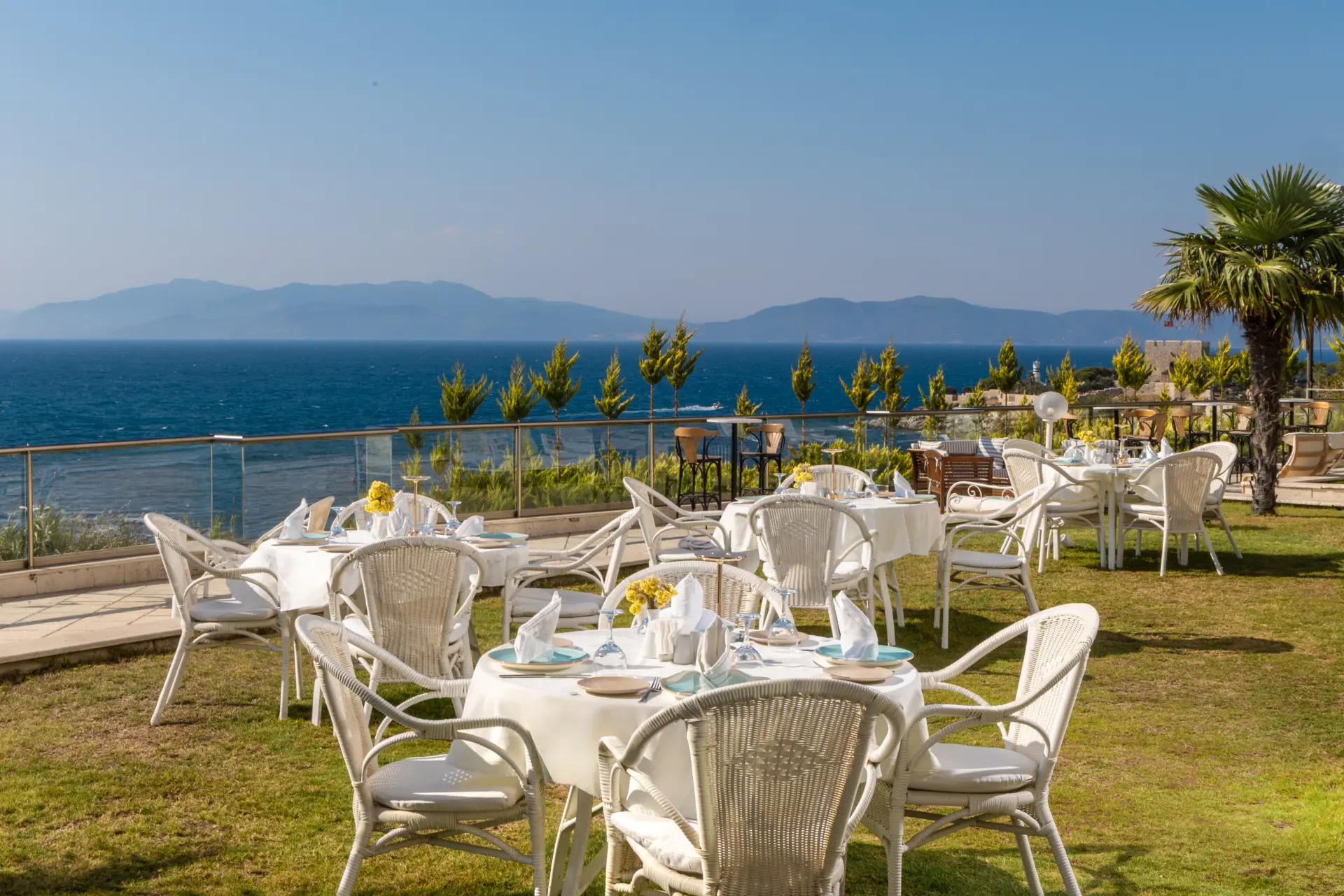 Güvercinada yönüne deniz manzaralı, çimenlikte kurulmuş teras restoran masaları